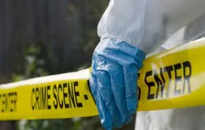 PPE-gloved hand behind crime scene tape for a death cleanup in Fresno, CA